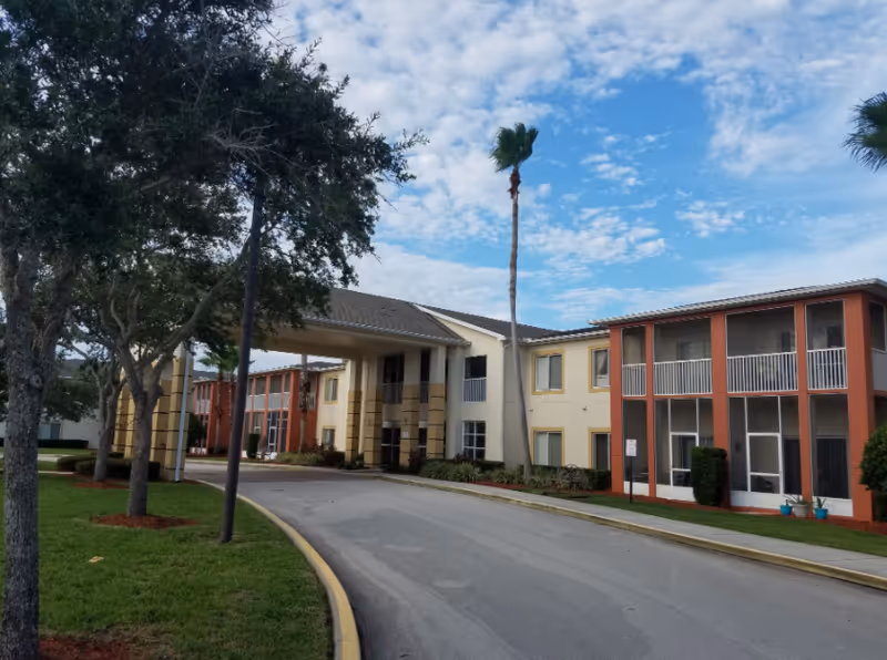 Exterior view of Century Oaks senior living campus with curved road and two-story buildings.