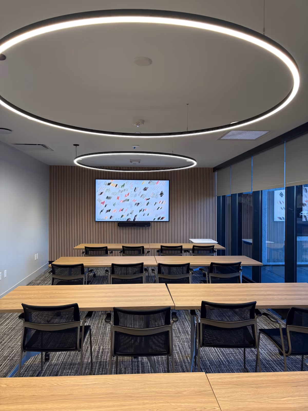 A modern conference room with circular ceiling lights, desks, and a wall-mounted screen.