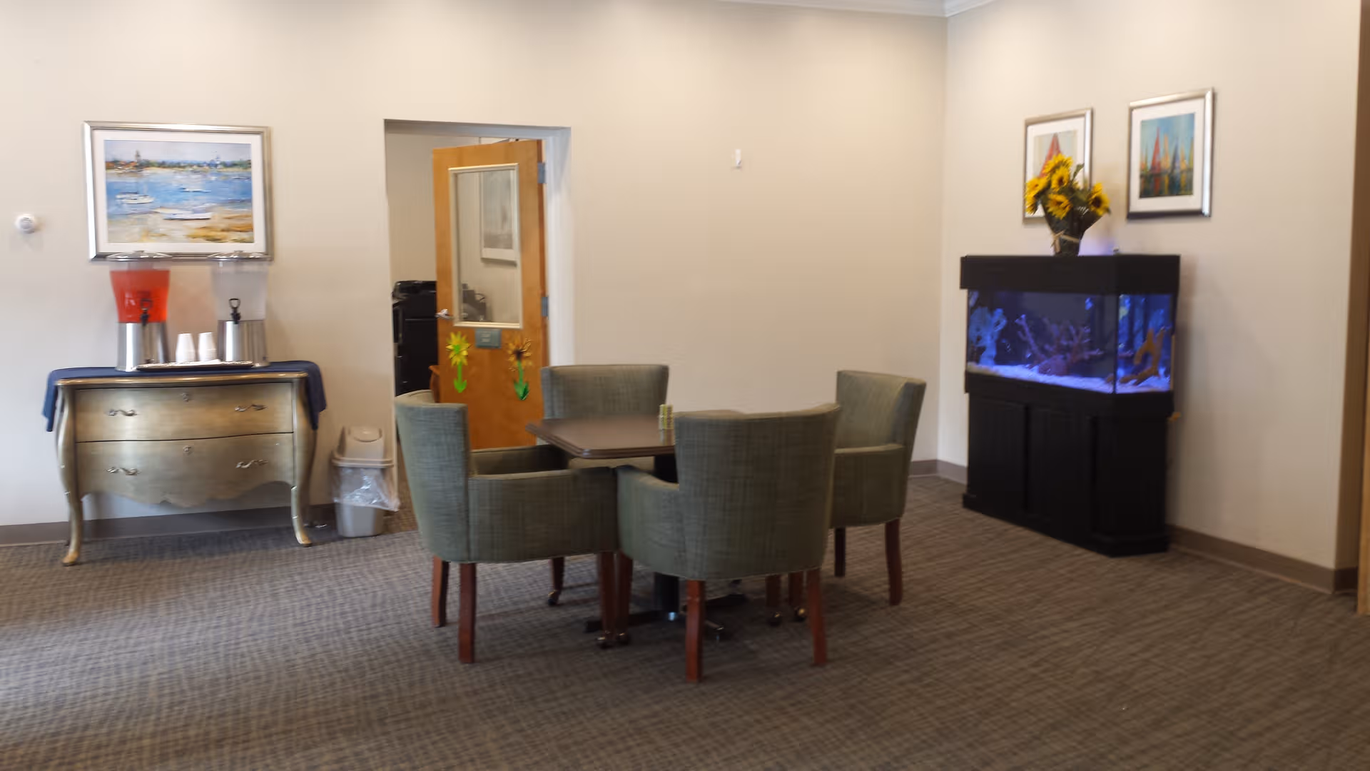 A lounge area with a round table, four green chairs, an aquarium, and a beverage station.