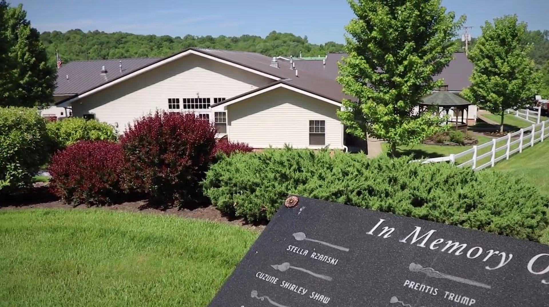 Exterior view of Hospice facility with landscaped grounds, a white fence, and a memorial plaque.