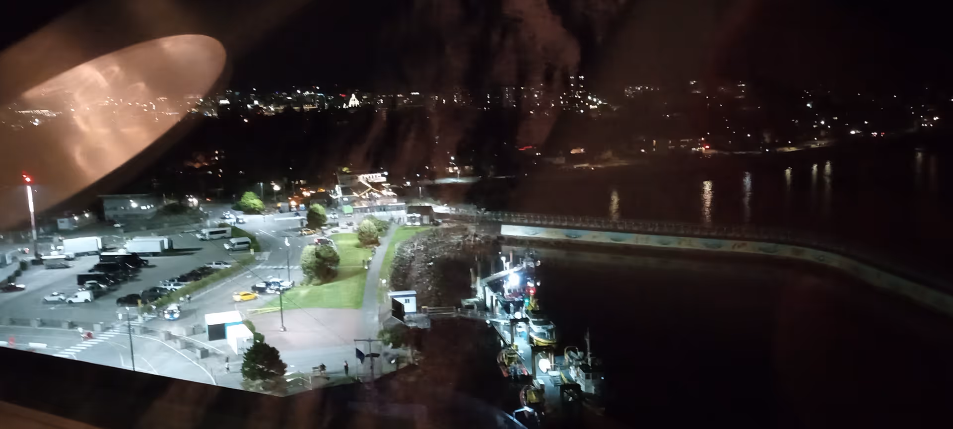 Nighttime harbor view with boats, water, and city lights from a high-rise.