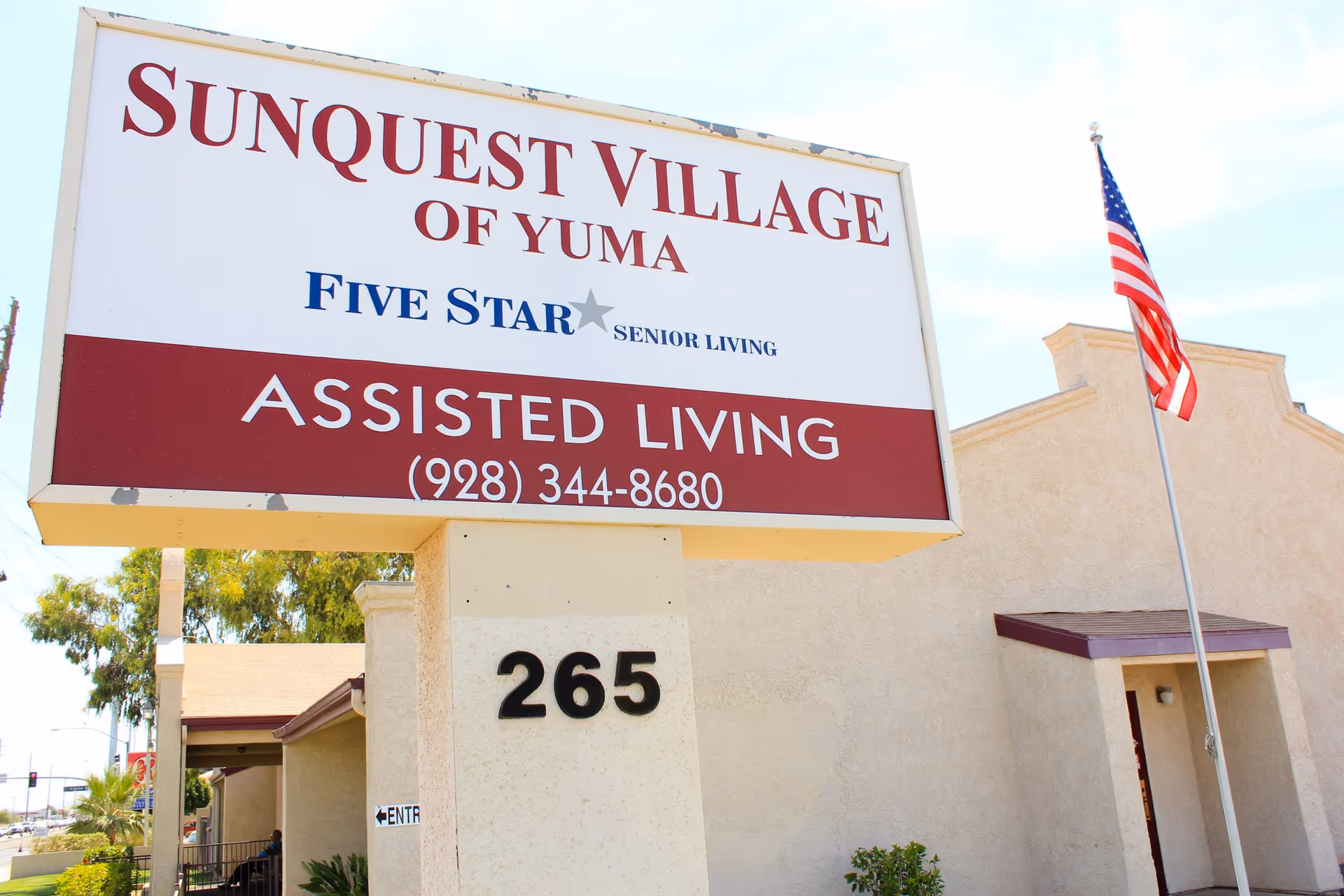 Front exterior of SunQuest Village of Yuma with a large sign and American flag.