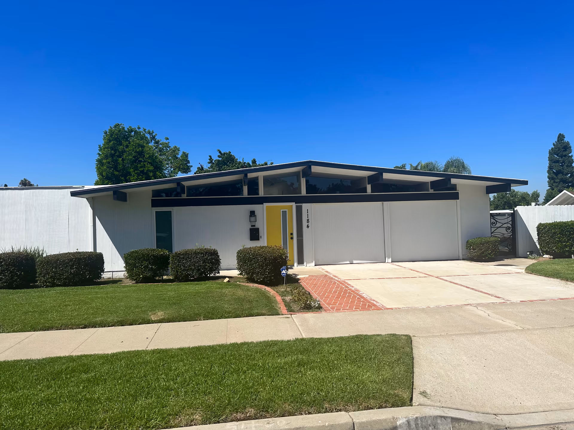 Residential-style single-story senior facility with white walls, a yellow door, and manicured shrubs.