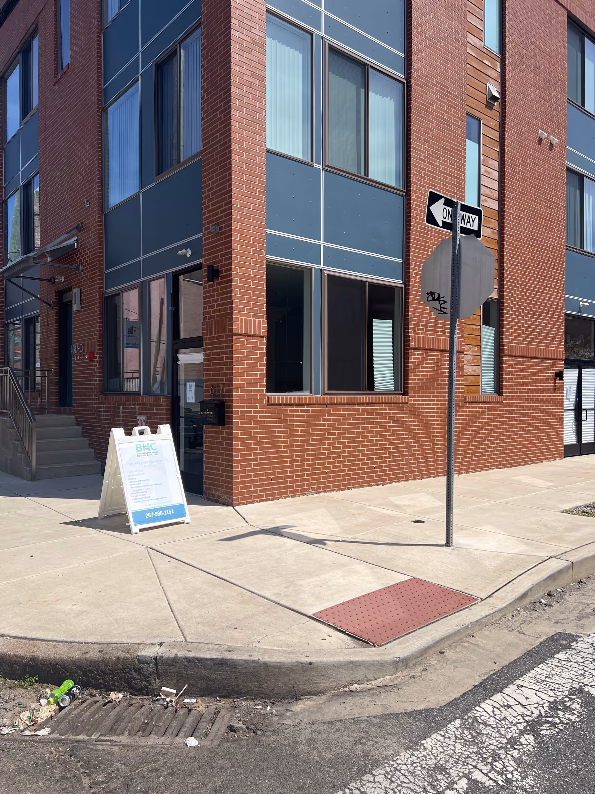Brick building corner with large windows, sidewalk, and an A-frame sign.
