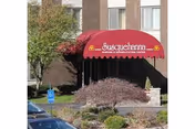 Red awning with Susquehanna Nursing and Rehabilitation Center entrance over shrubs and a parked car.