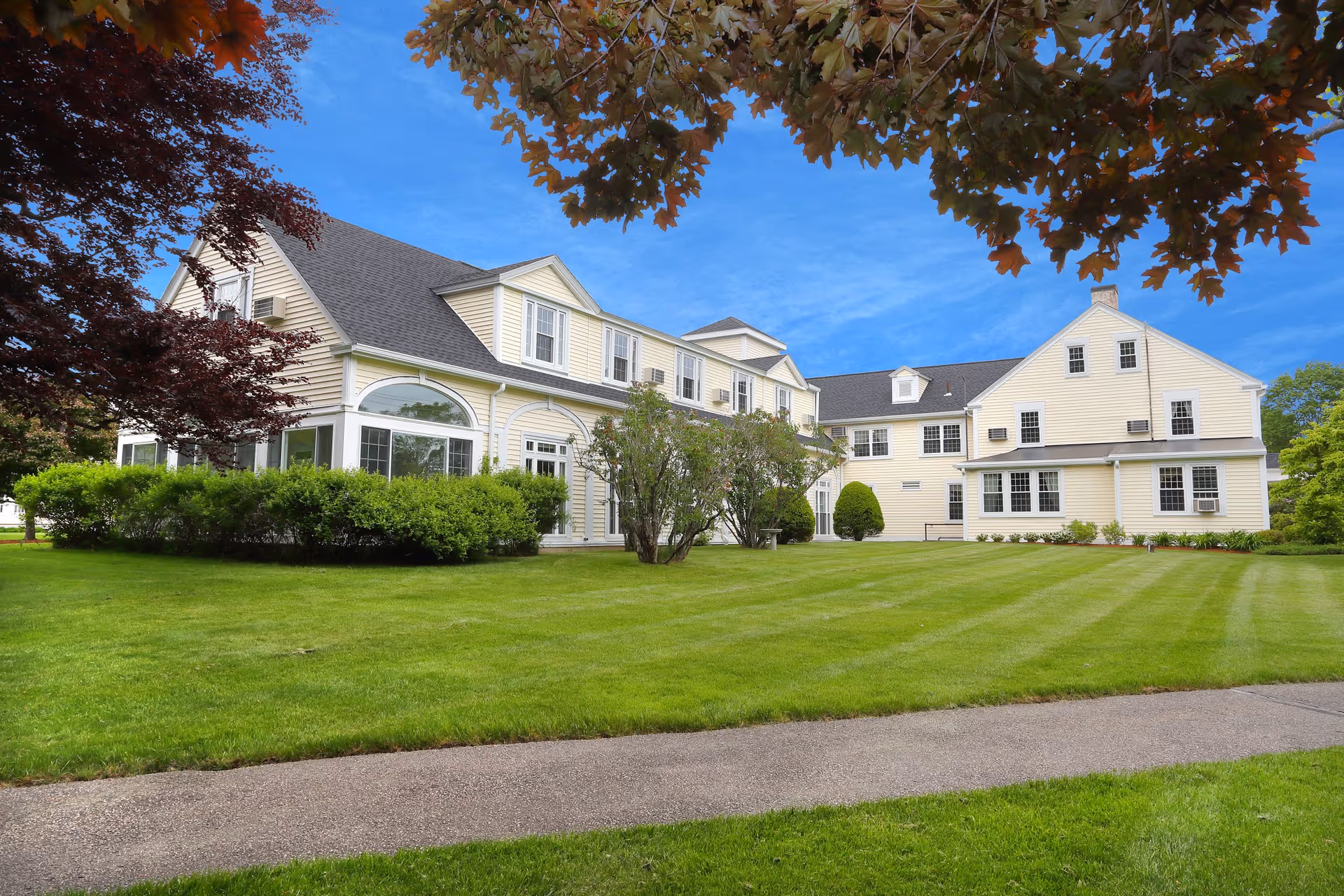 Front exterior of a large yellow two-story building with a manicured lawn and trees.