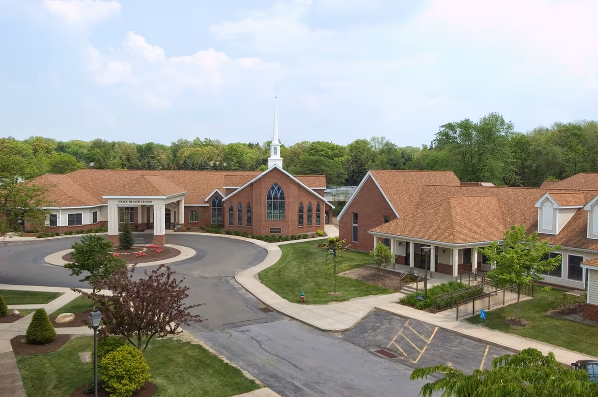 Brick senior living center with circular driveway and front entrance, surrounded by trees.