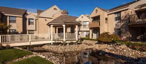 Exterior view of Waltonwood University senior living campus with gazebo beside a pond.