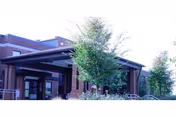 Brick-front senior living facility entrance with a covered porte-cochère and trees.