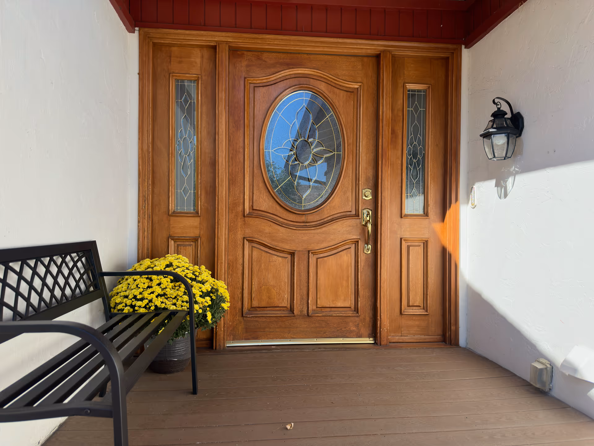 Front wooden door with decorative glass, a bench, and yellow flowers on the porch.