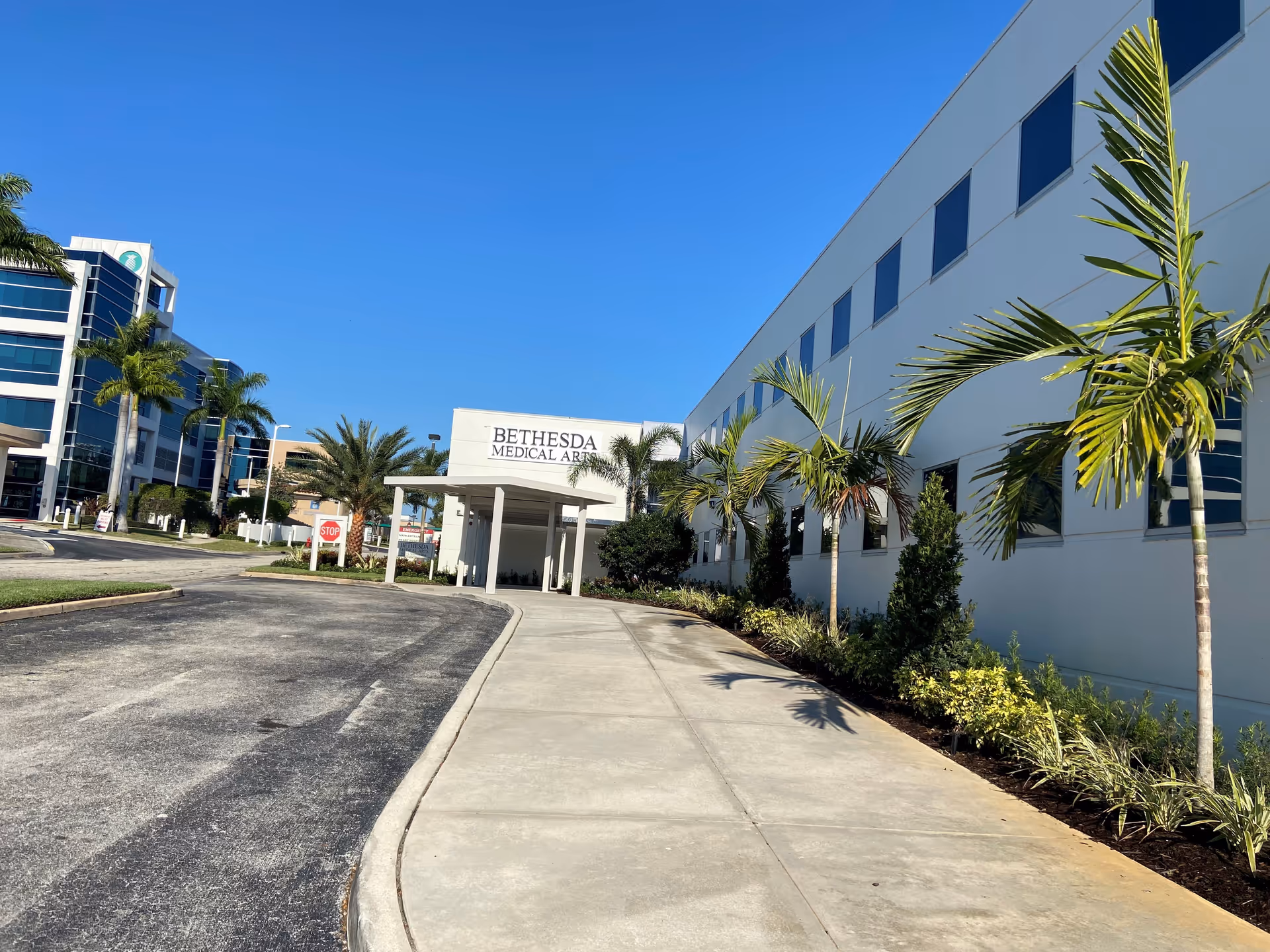 Exterior view of a modern medical facility with a walkway and palm trees.