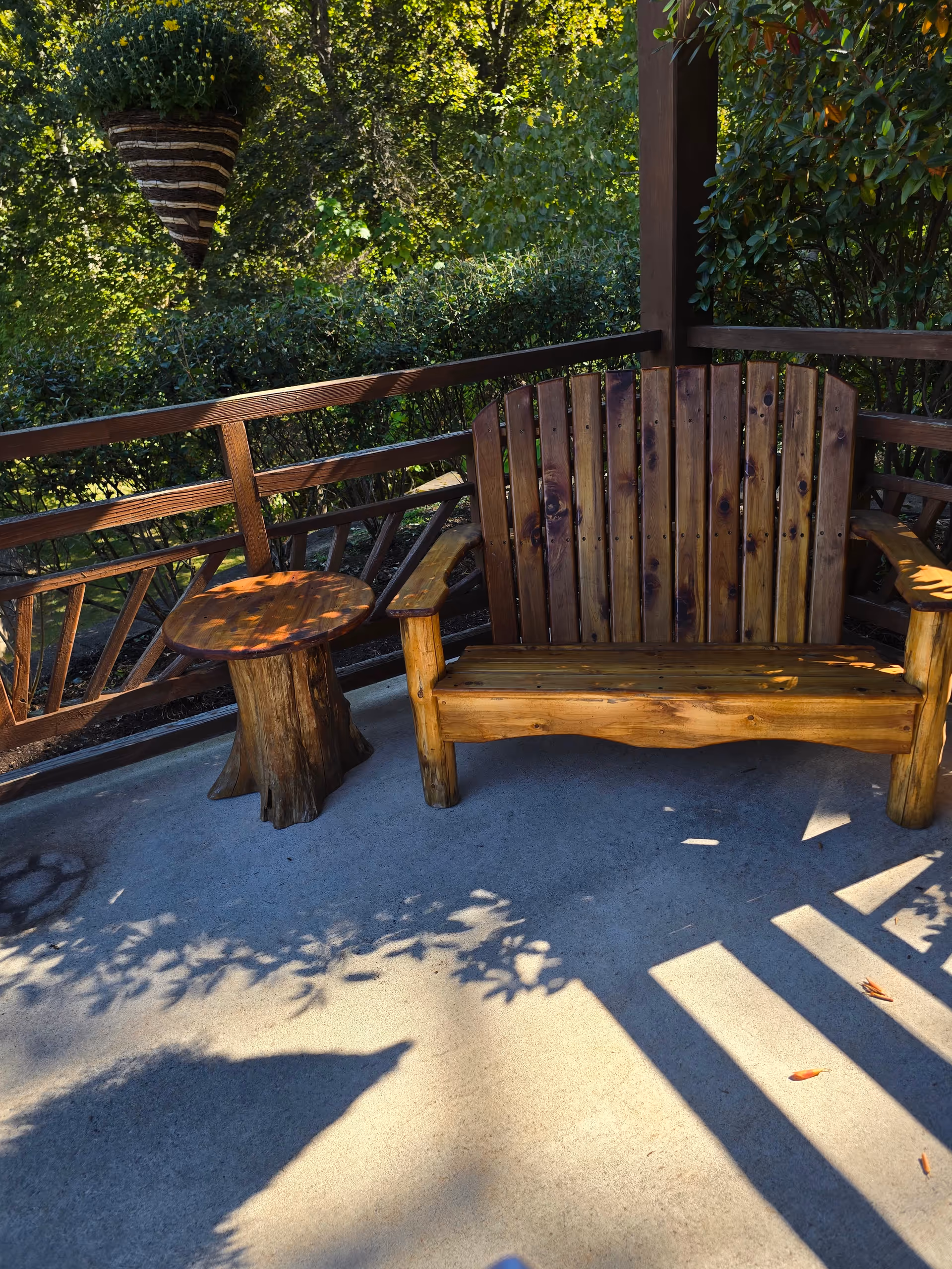 Wooden outdoor seating area with a bench and round table on a sunlit patio.