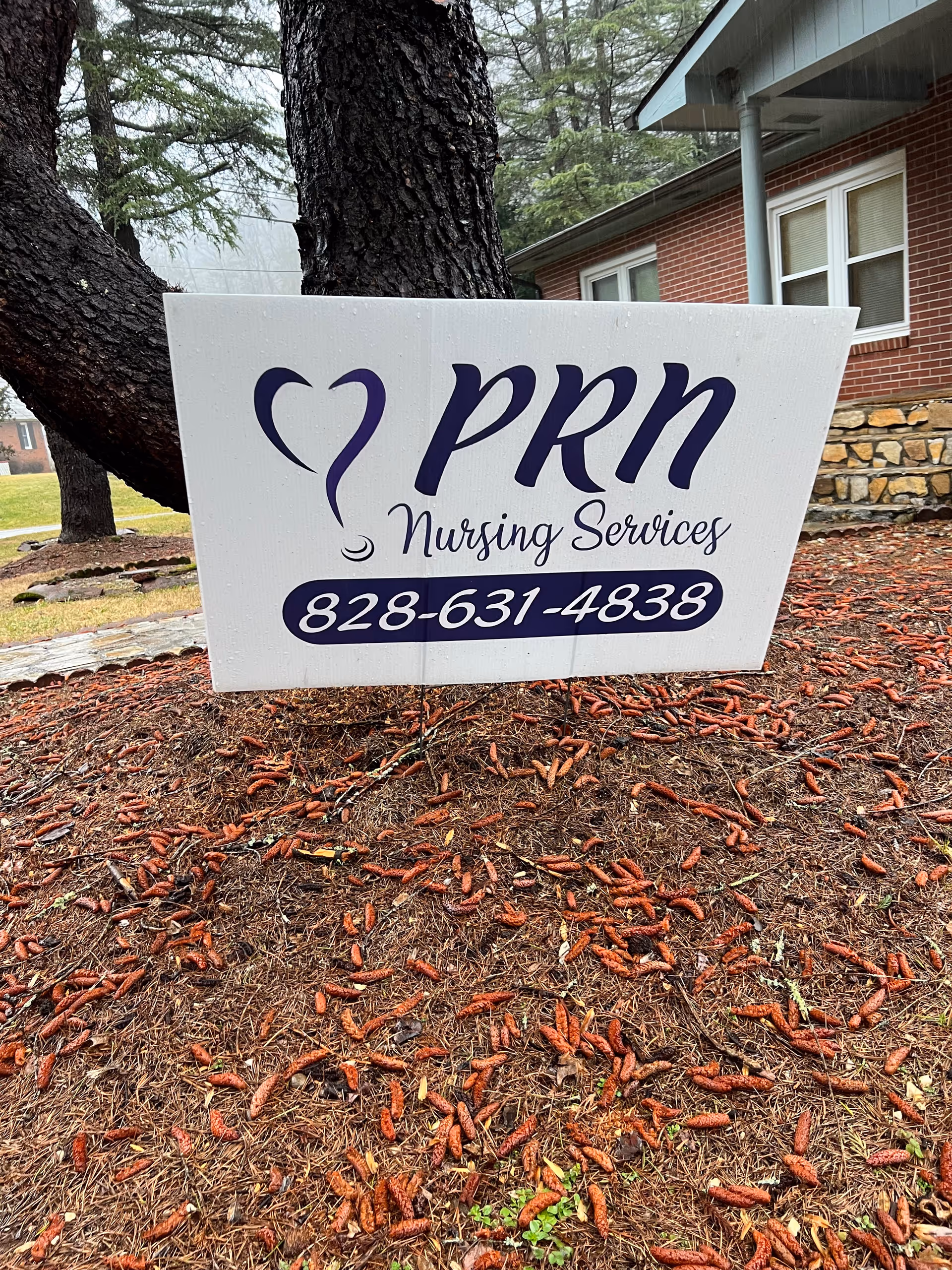 A PRN Nursing Services sign sits on mulch near a brick building.