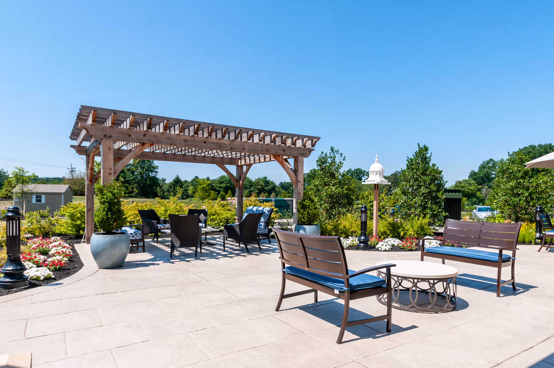 Outdoor patio on a sunny day with seating under a wooden pergola.