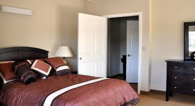 A tidy bedroom with burgundy bedding, nightstand lamp, dresser, and open door.