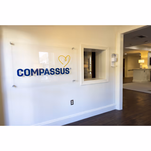 White interior wall with a Compassus sign, window opening, and distant reception area.