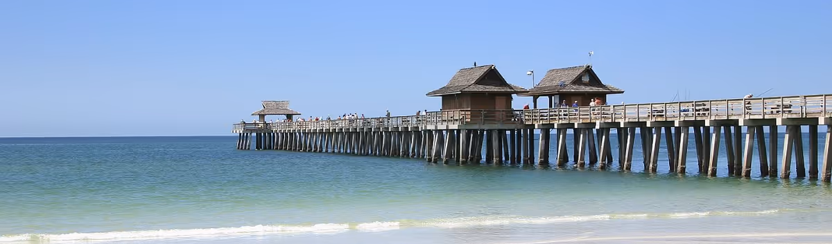 A long wooden pier stretches into the calm blue sea with thatched-roof pavilions.