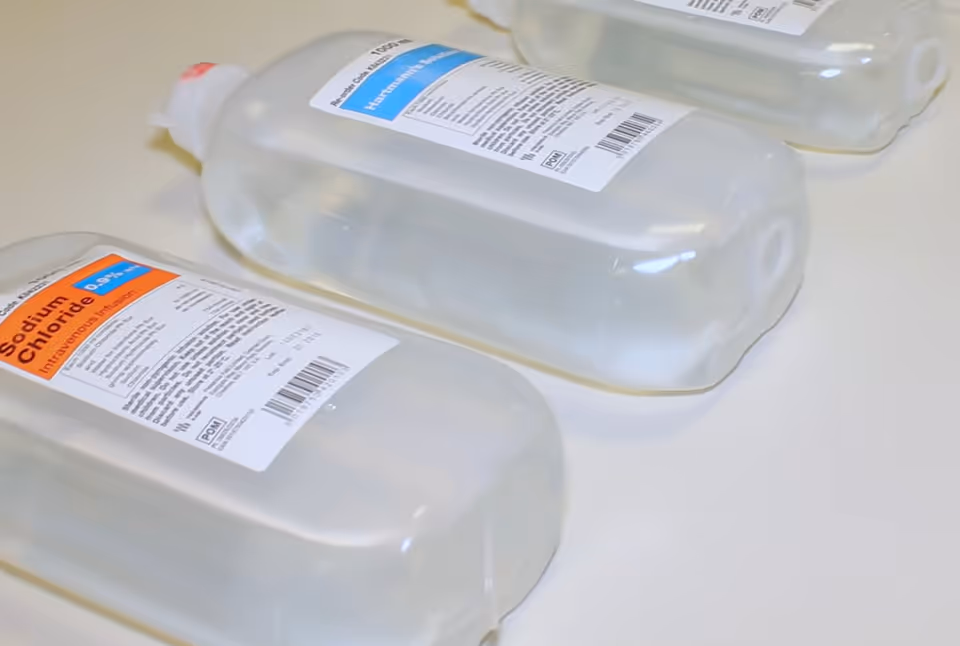 Clear plastic IV bags labeled saline on a white clinical countertop at a facility.