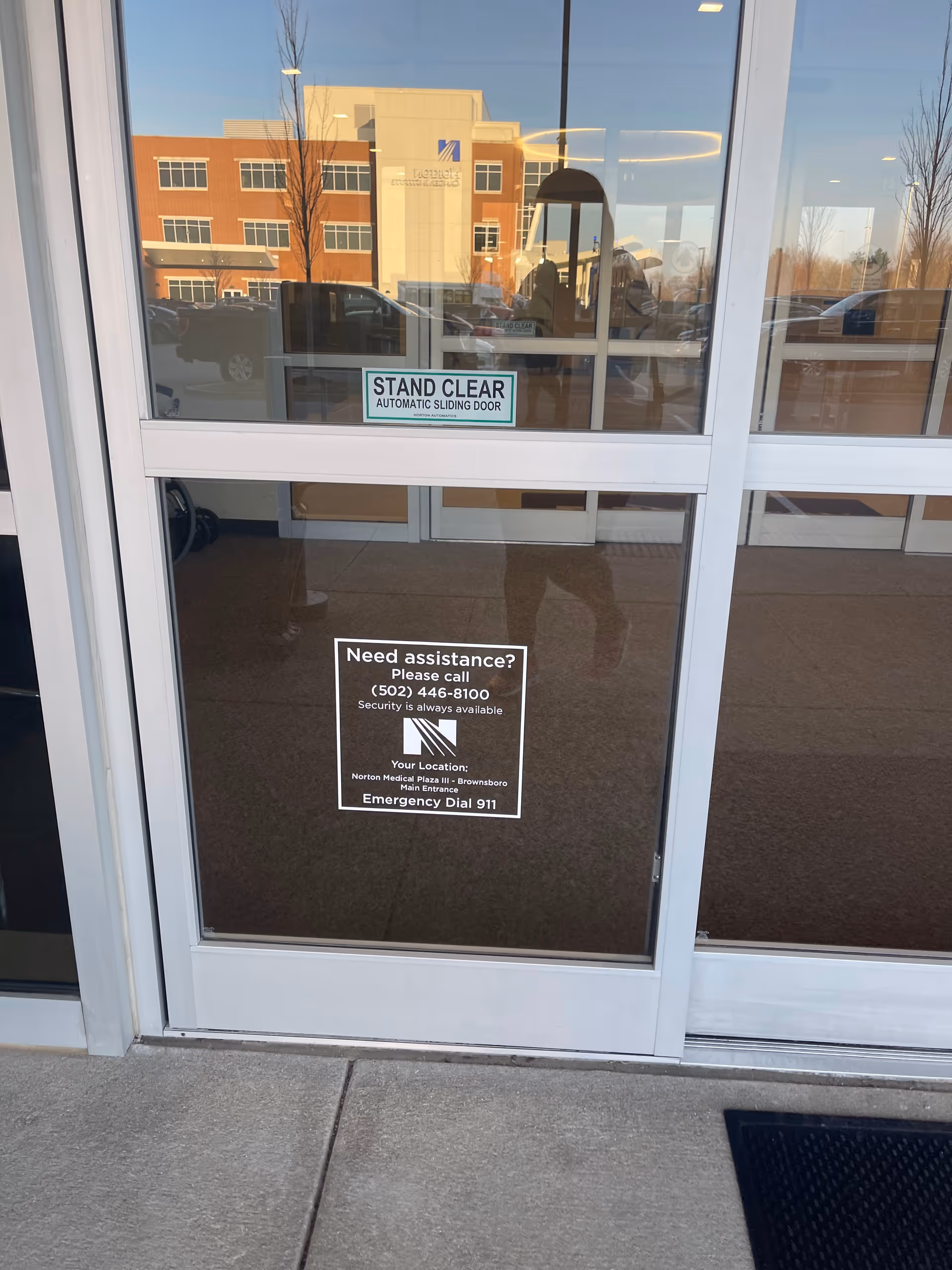 Glass automatic sliding doors show Norton Healthcare signage at the Brownsboro medical plaza entrance.