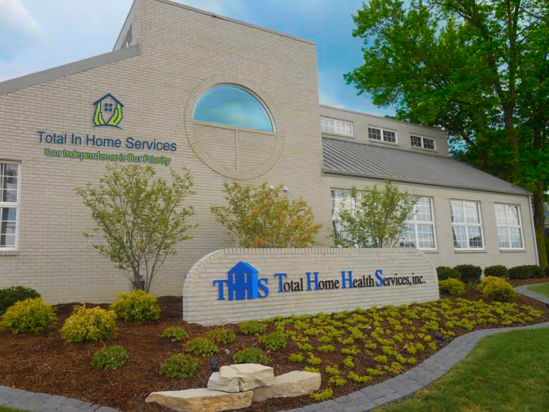 Beige brick building front with Total In Home Services sign and landscaped garden.