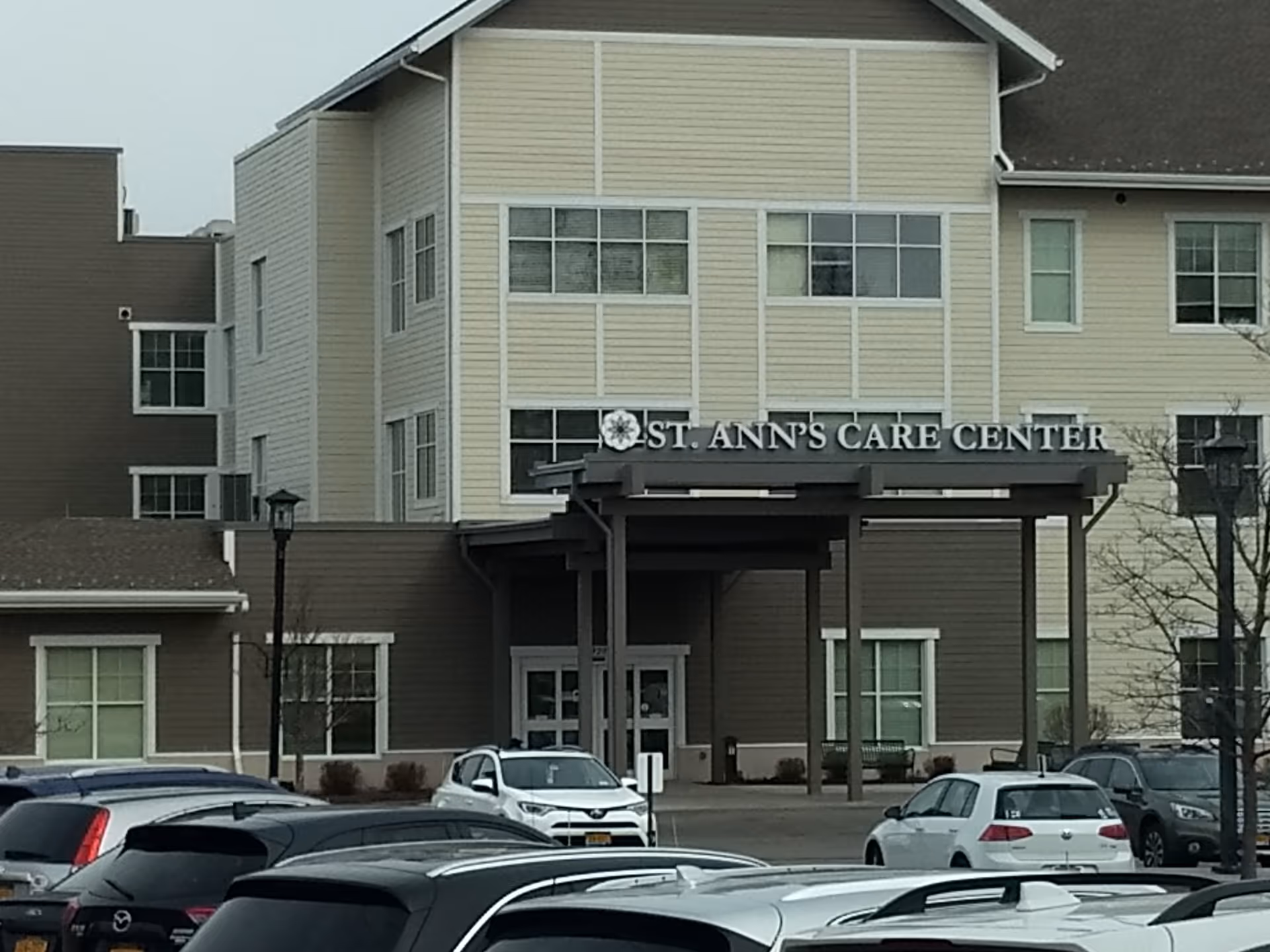 Exterior view of St. Ann's Care Center entrance with several parked cars.