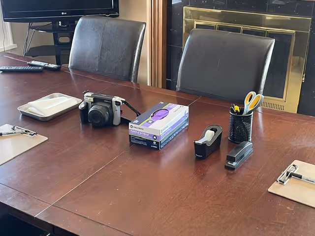 Conference table with camera, tissue box, stapler, scissors, and office supplies near a fireplace.