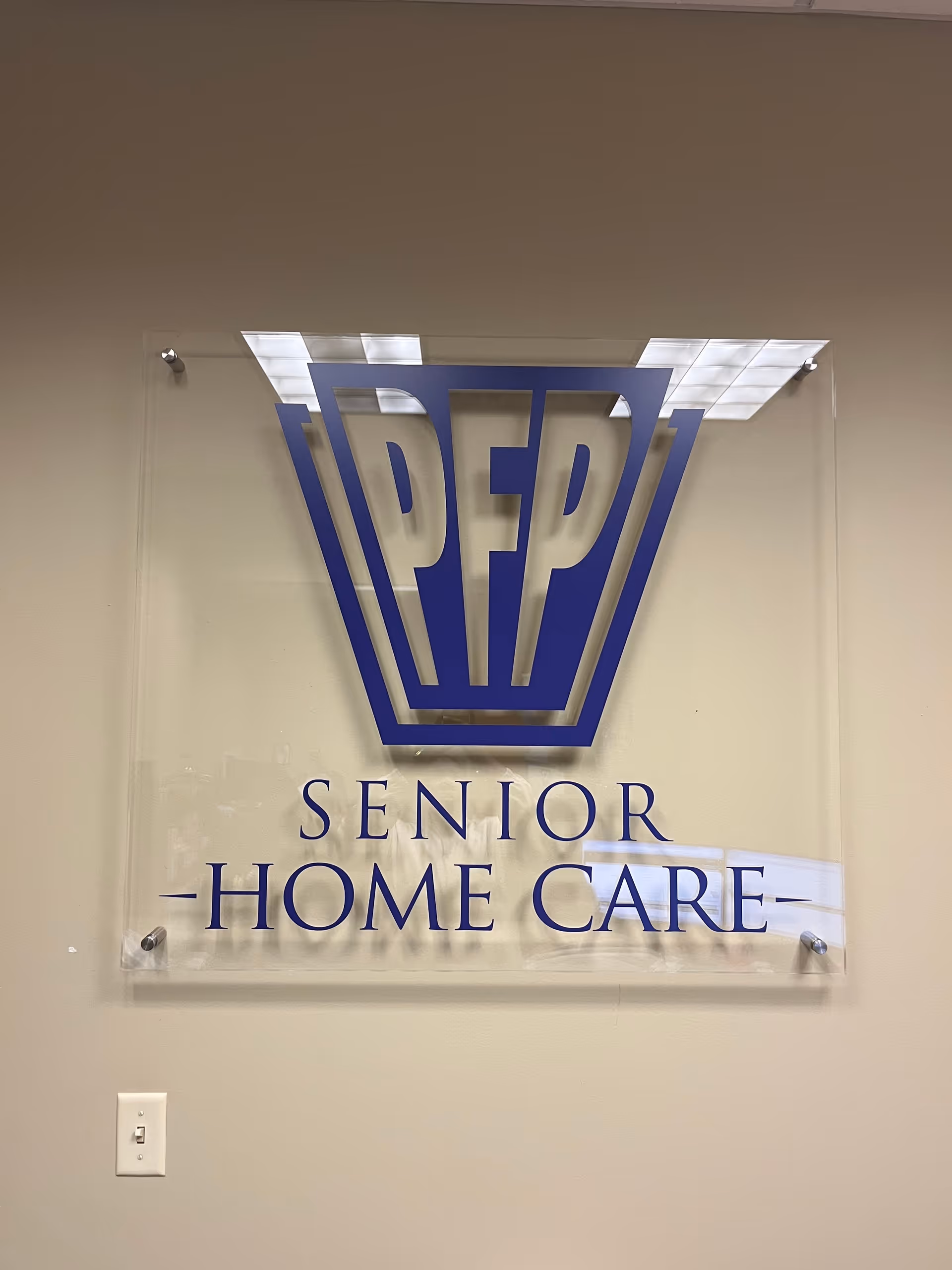 Clear acrylic sign on a wall displaying the PFP Senior Home Care logo.