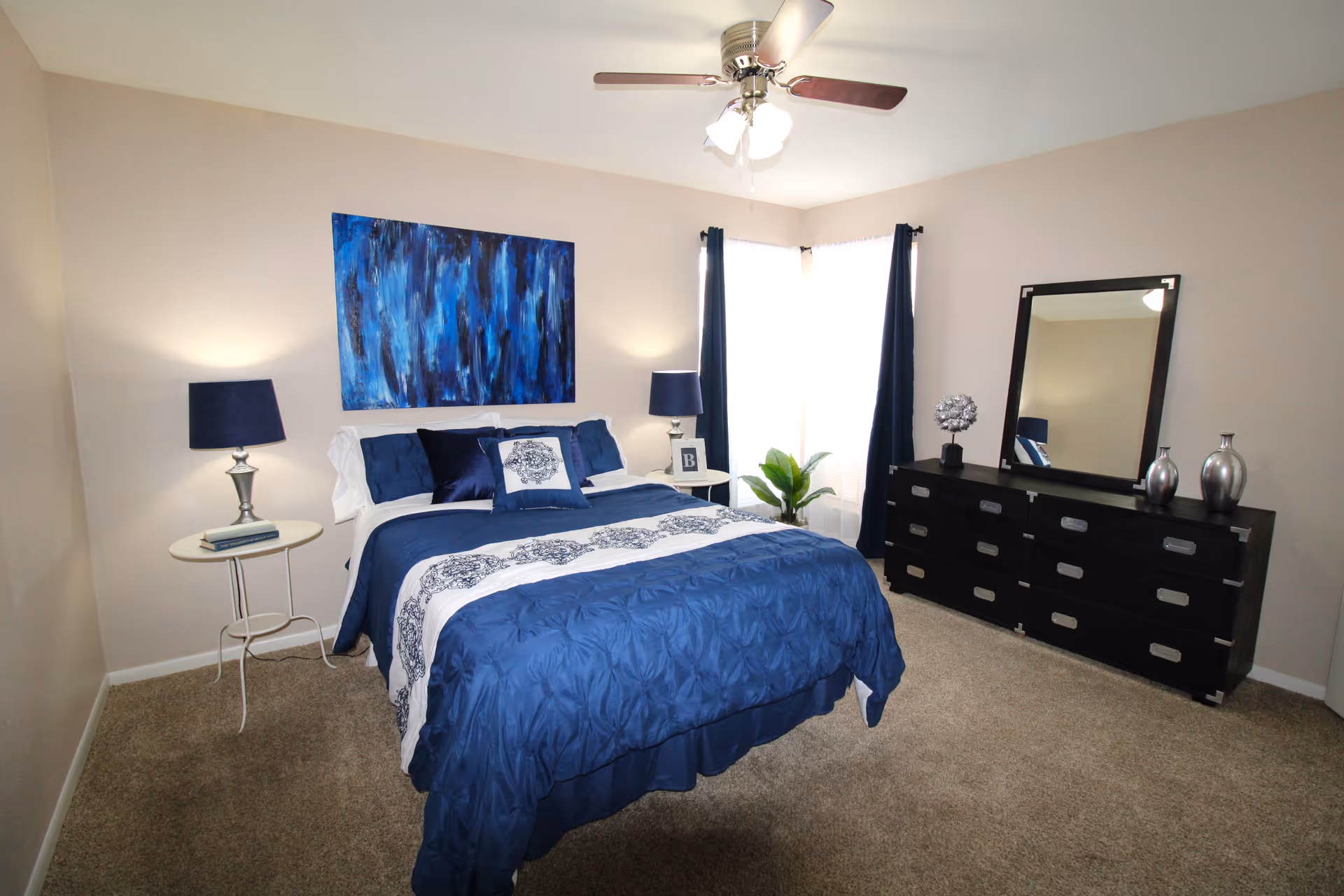 A neatly made blue-themed bedroom with bed, two nightstands, dresser, mirror, and ceiling fan.
