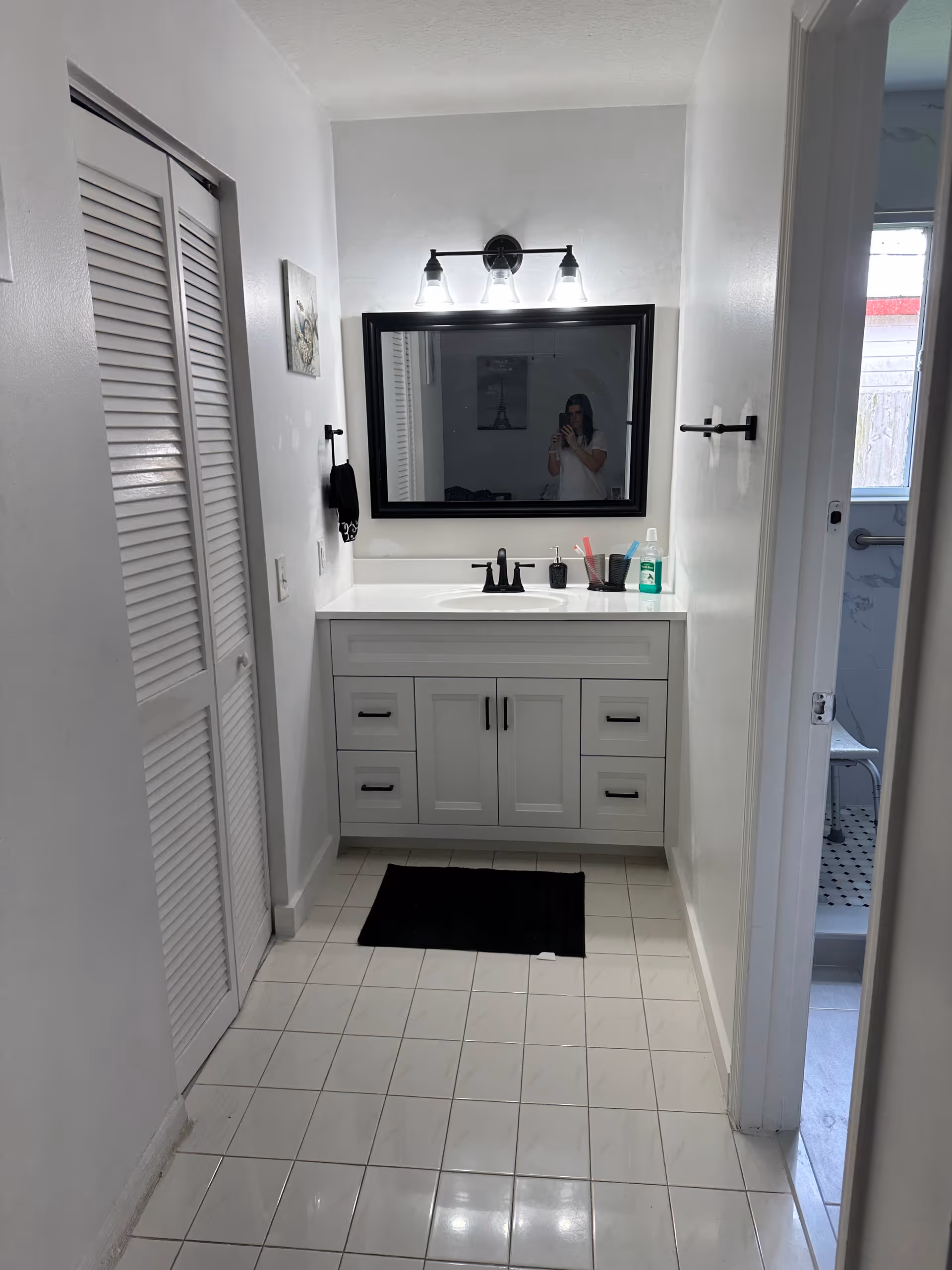 Bathroom with white vanity, sink, large mirror, and bright three-light fixture.