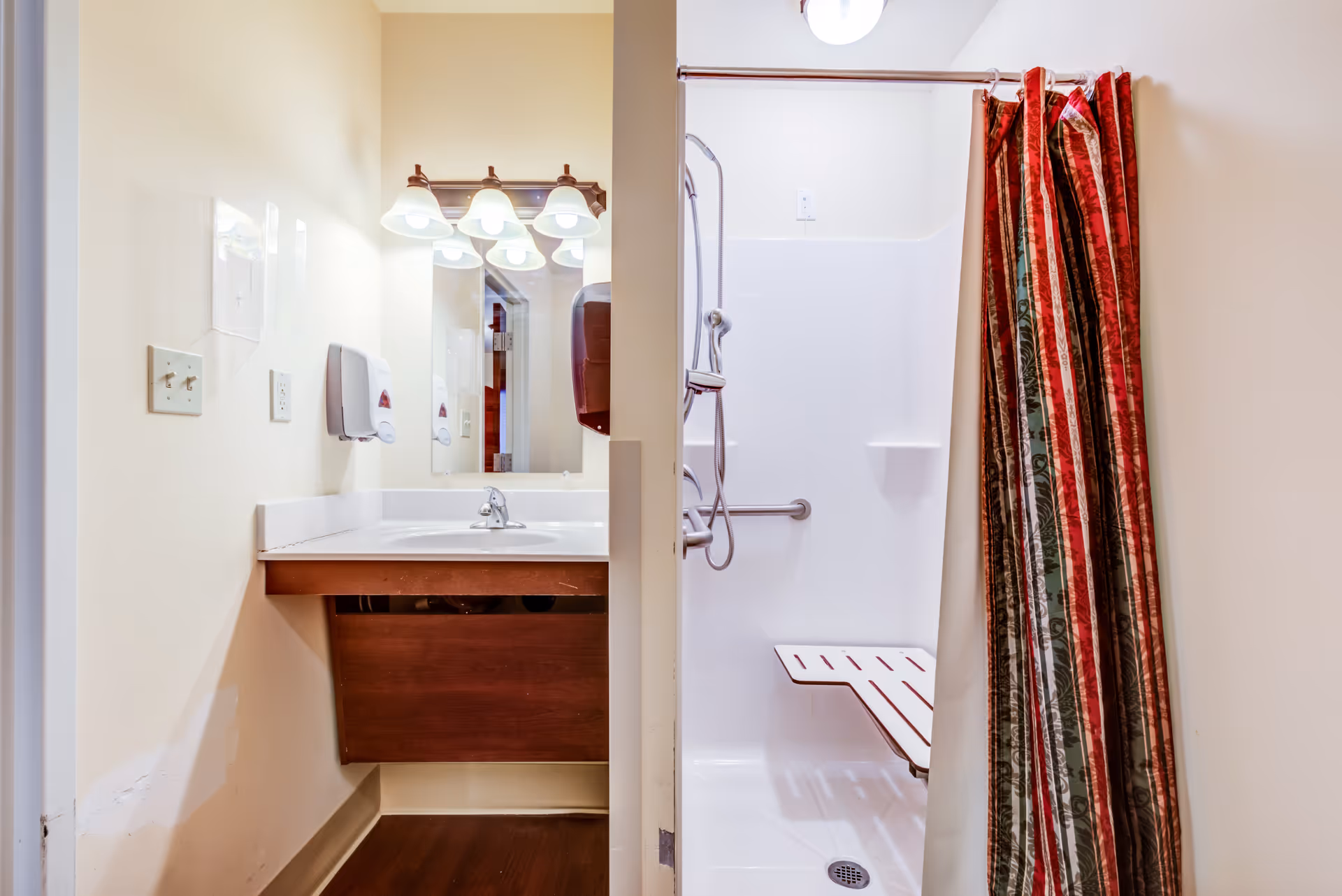 Bathroom with sink, mirror, and accessible shower stall featuring a red striped curtain.