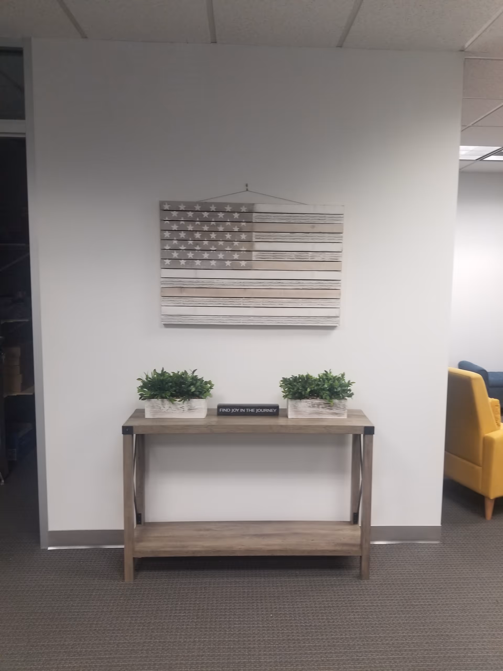 A wooden console table with two potted plants and wall art in a neutral interior.
