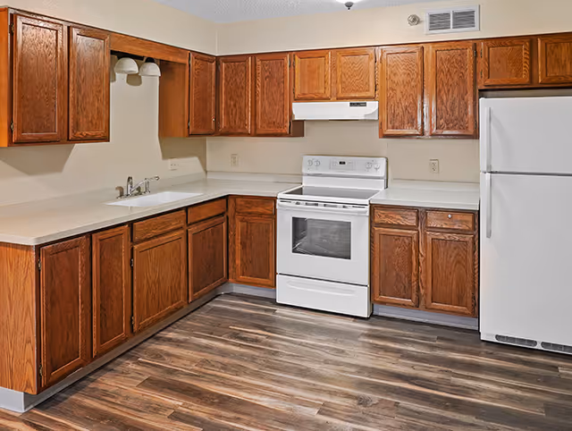 Kitchen in a senior living facility with wooden cabinets, white appliances, and laminate flooring.