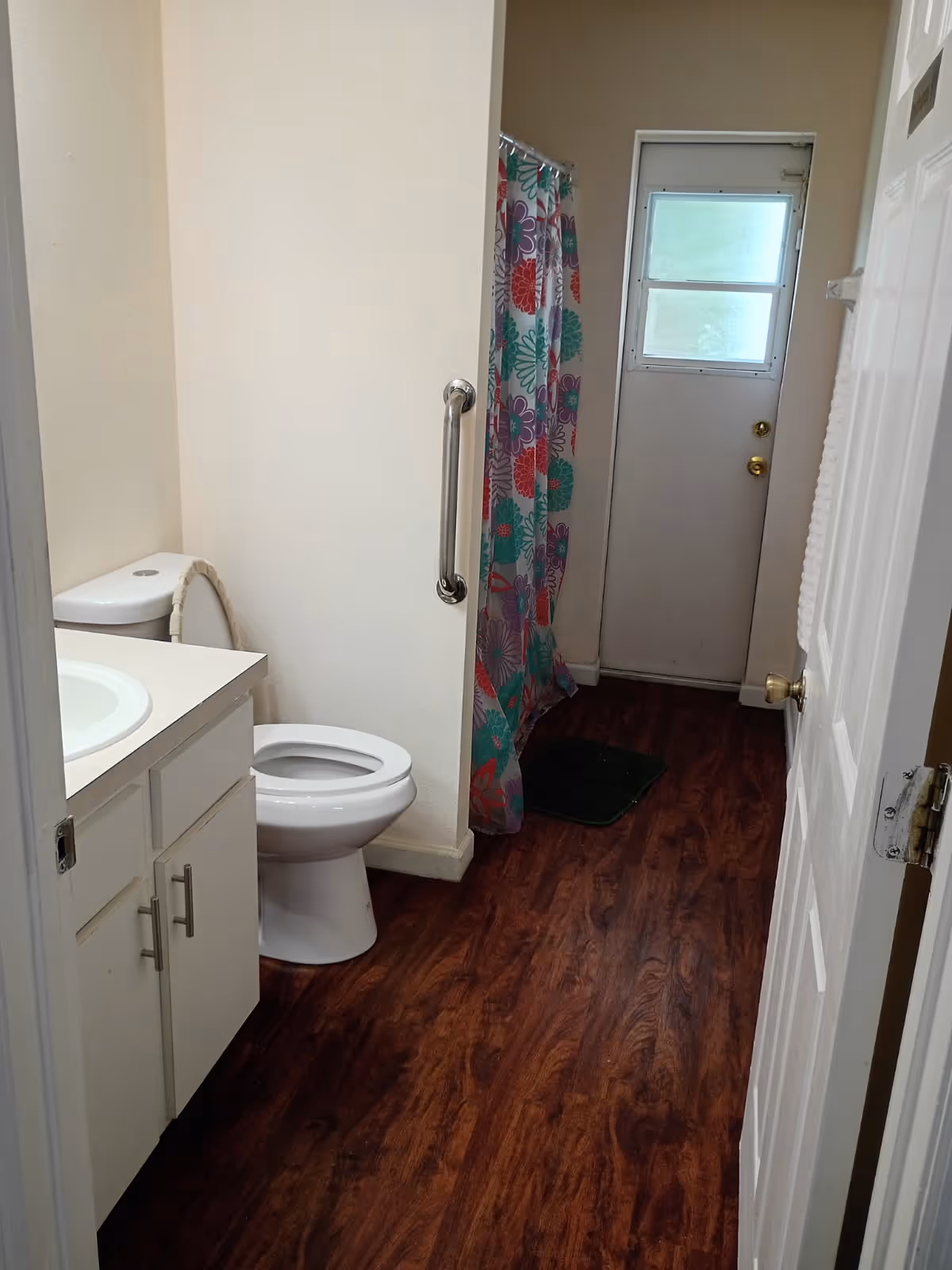 Compact bathroom featuring sink, toilet, shower curtain, wood-like floor, and doorway.