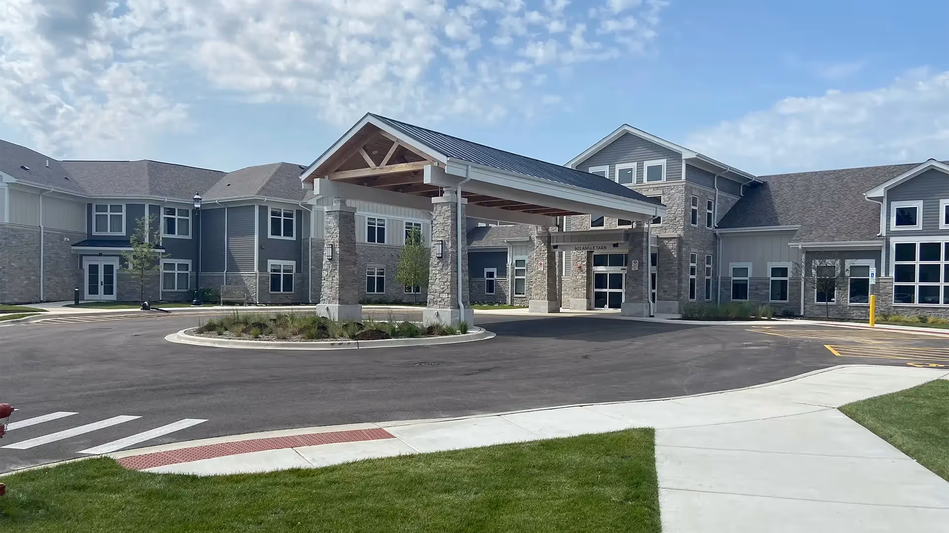 Front exterior of The Woodlands at Canterfield showing a covered entrance/porte-cochere, circular driveway, and surrounding lawn and building facade.