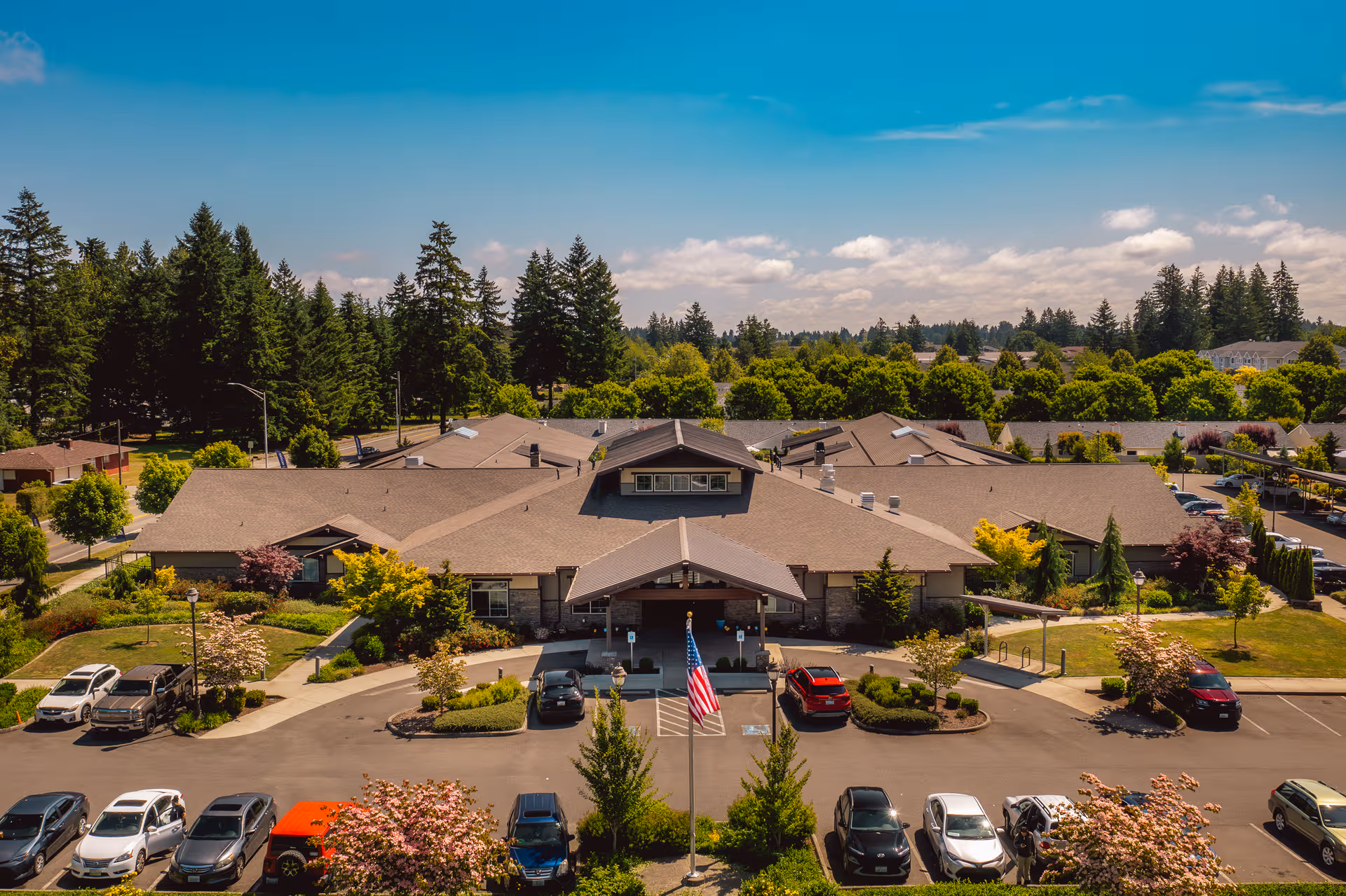A large, single-story building with a central entrance, parking lot, and trees.