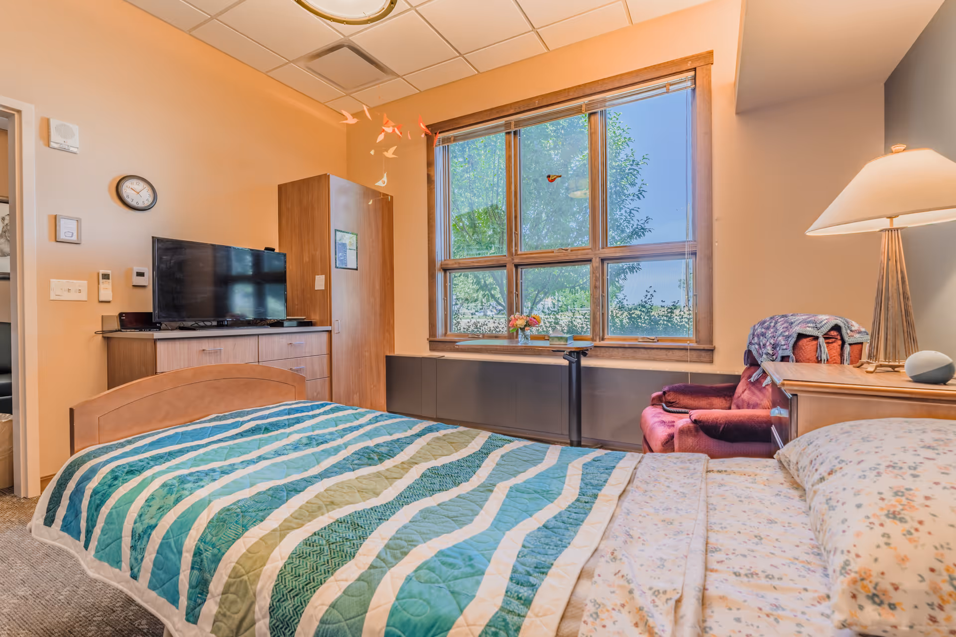 Cozy senior living bedroom with a bed, dresser, window, and TV.
