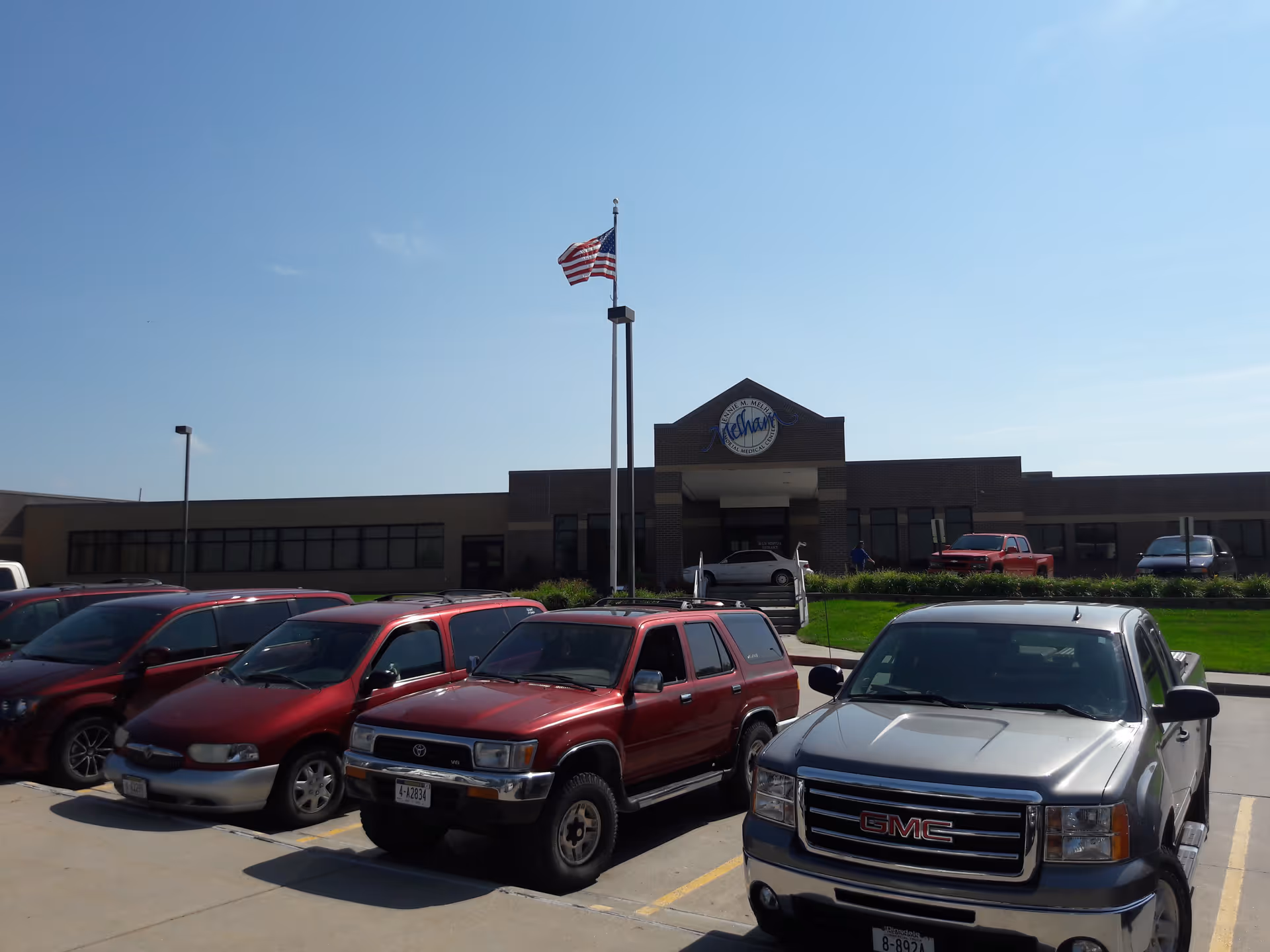 Front view of Jennie M. Melham Memorial Medical Center with parked cars and American flag.