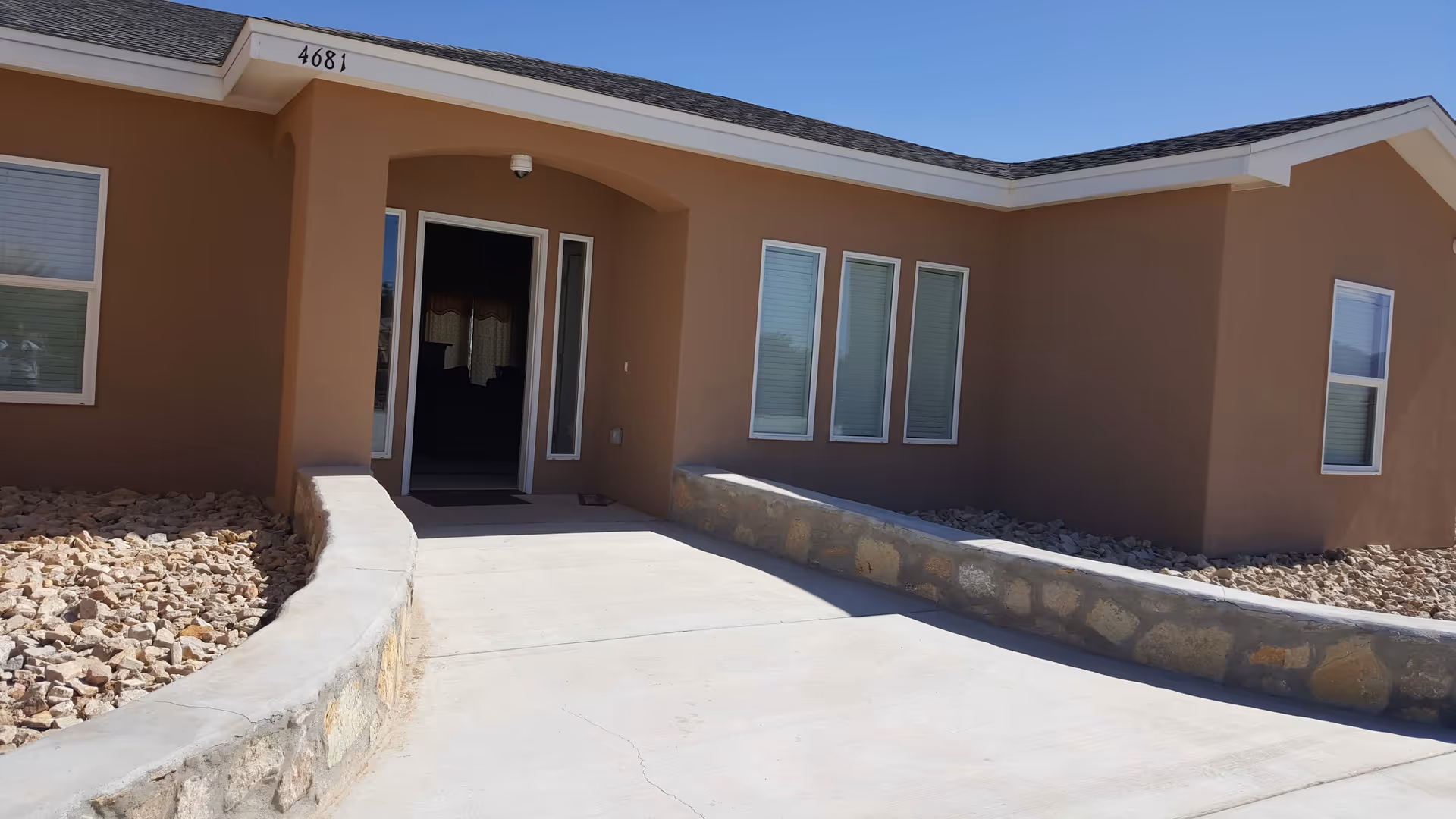 Single-story tan building with glass entry door, curved walkway, and rocky landscaping.