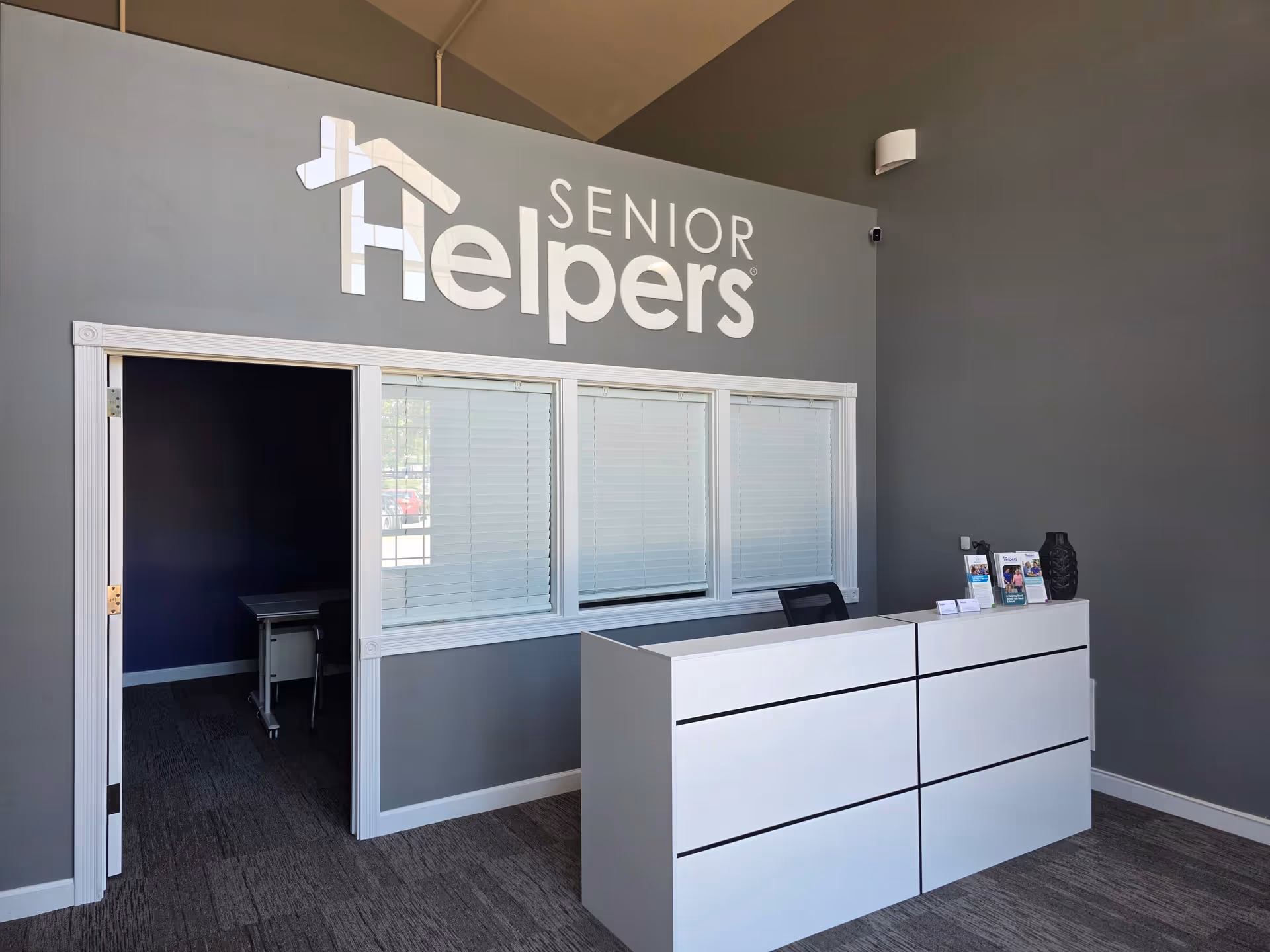 Reception area with a white desk, windows, and Senior Helpers sign on gray wall.