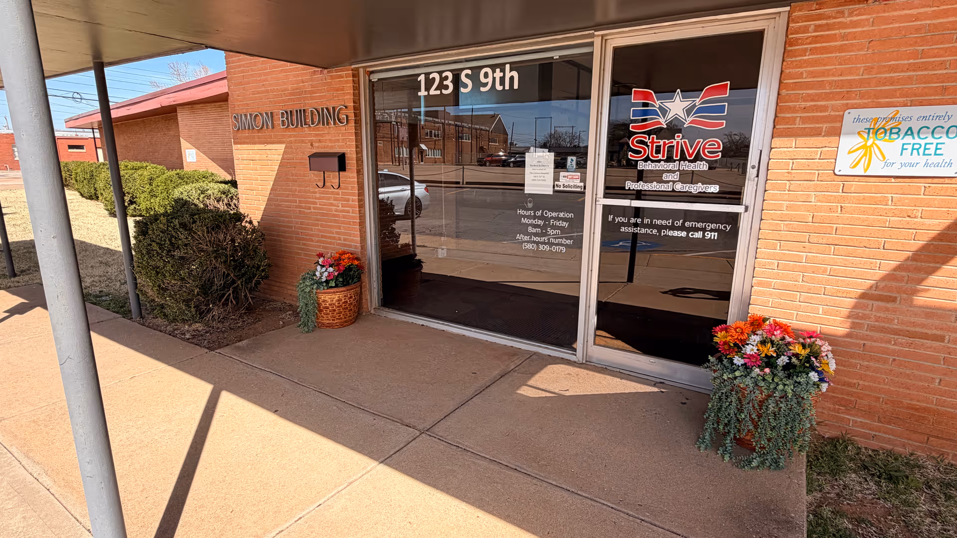 Brick building entrance with glass doors, Strive logo, and flowering planters.
