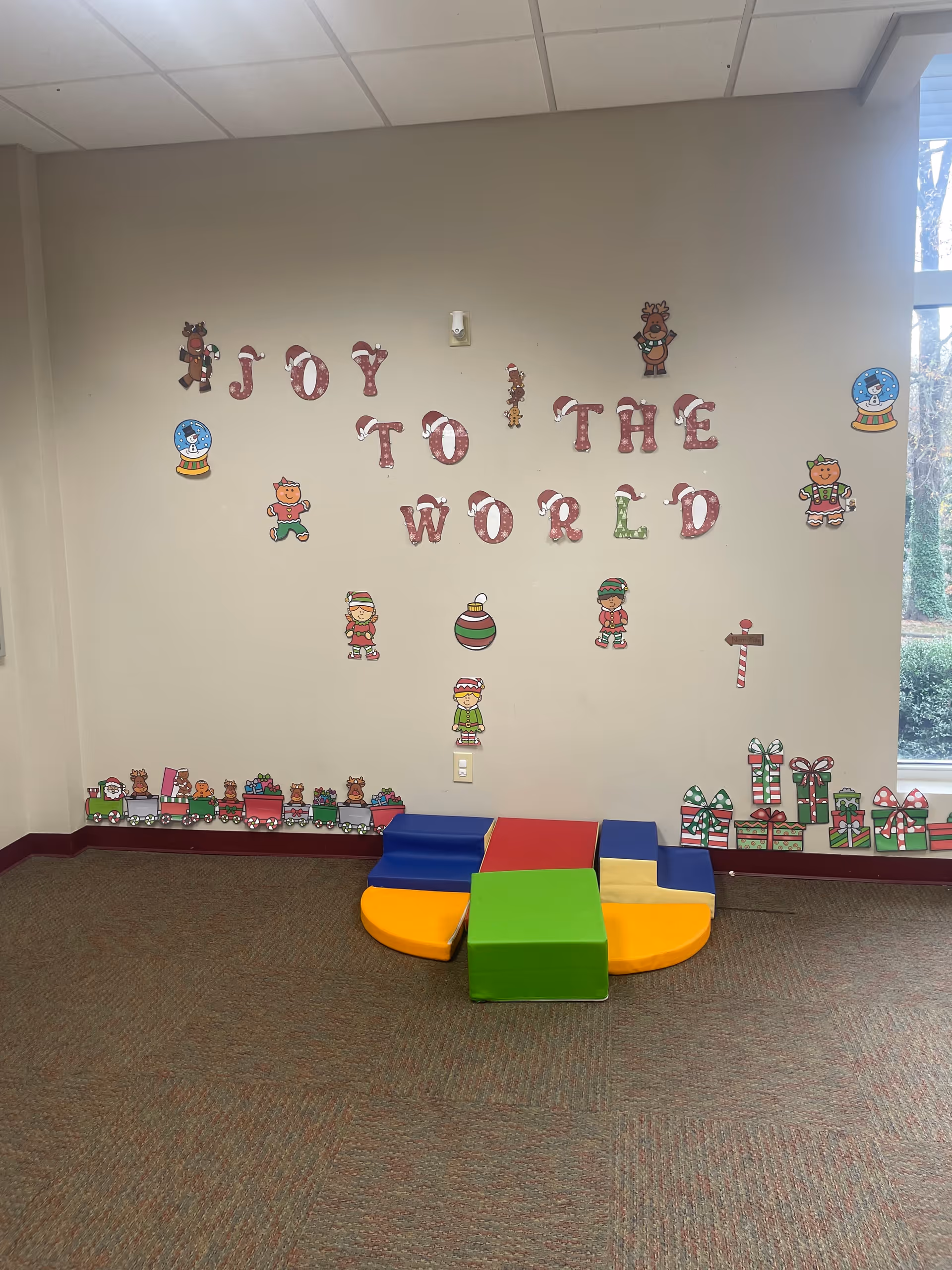 Colorful children's play area inside a facility with wall decorations and soft seating.