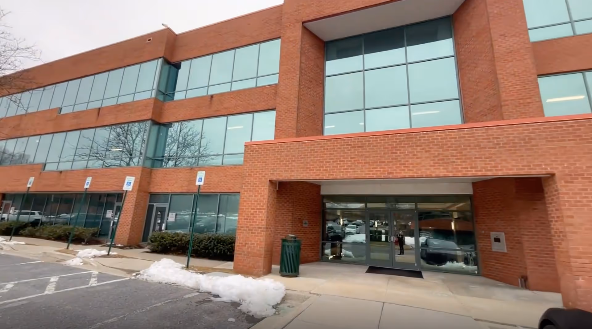 Brick office building with large glass windows and a glass entrance, surrounding parking lot.