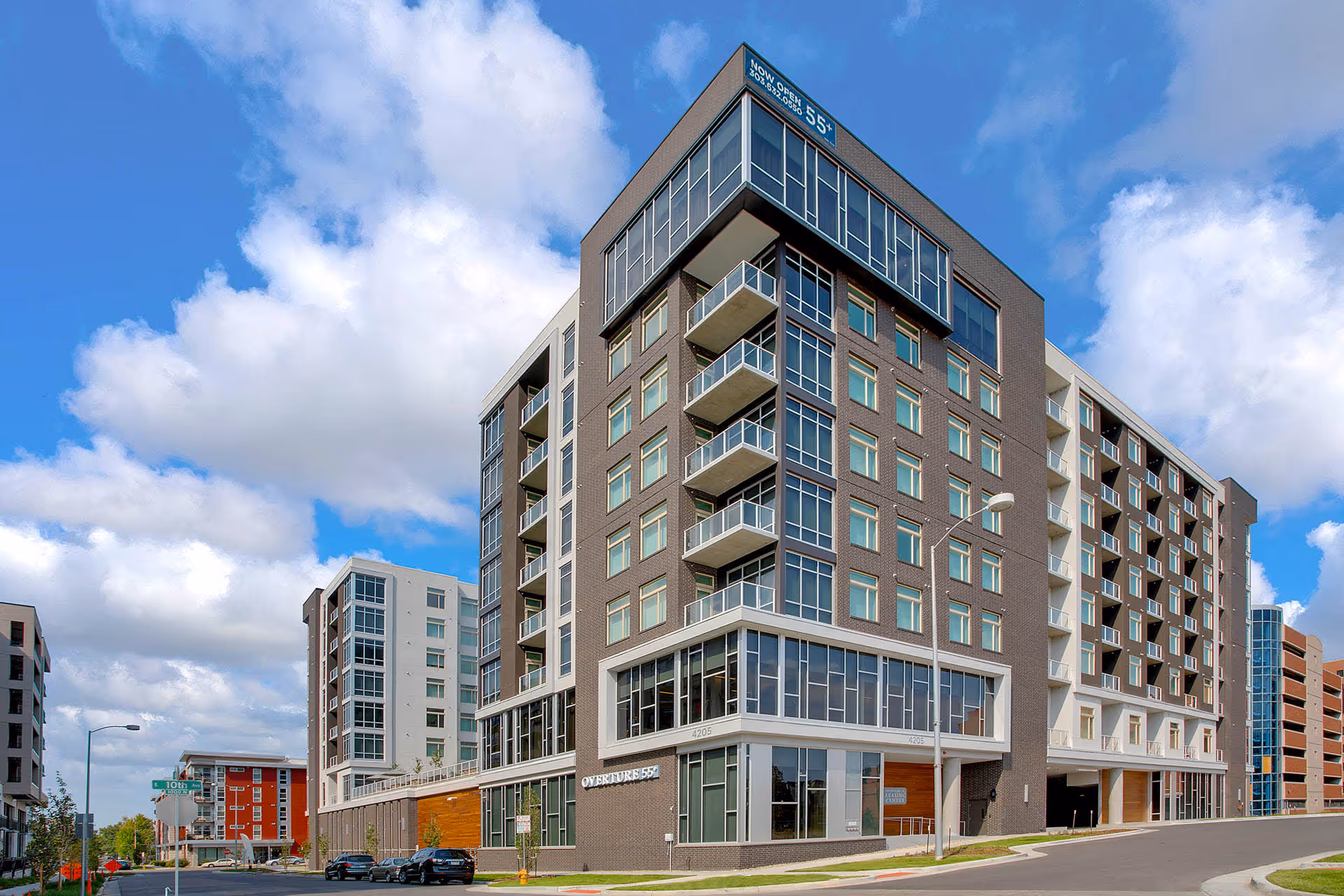 Exterior view of a modern multi-story apartment building with balconies and large windows under a partly cloudy sky.