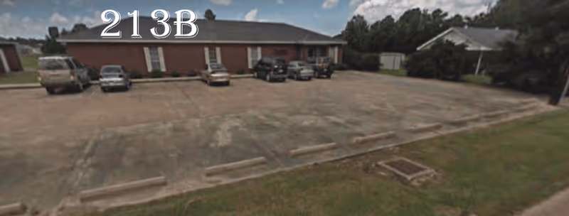 Brick facility with parked cars in front and a grassy area nearby