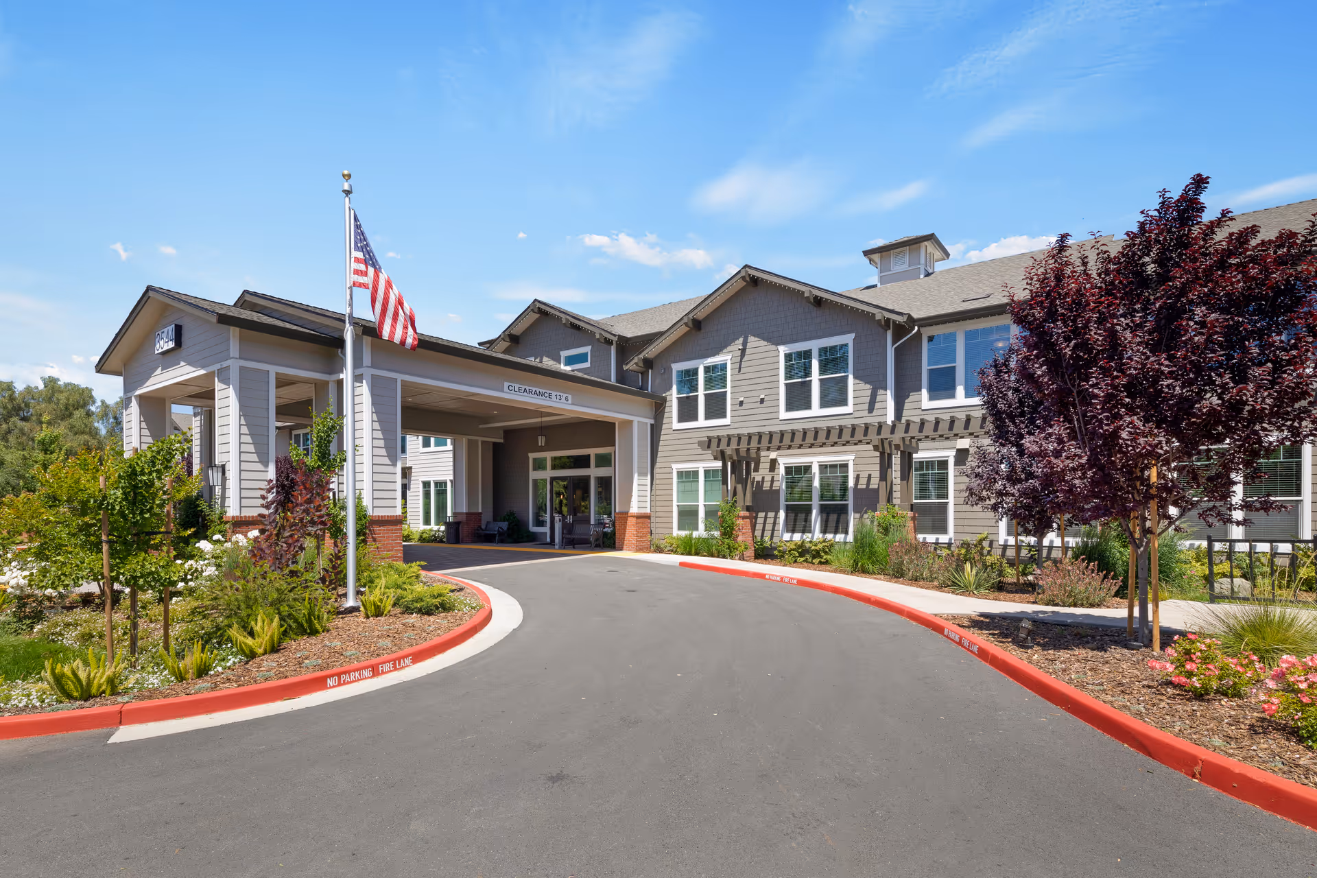 Exterior view of Oakmont of Silver Creek entrance with curved driveway, flagpole, and landscaping.