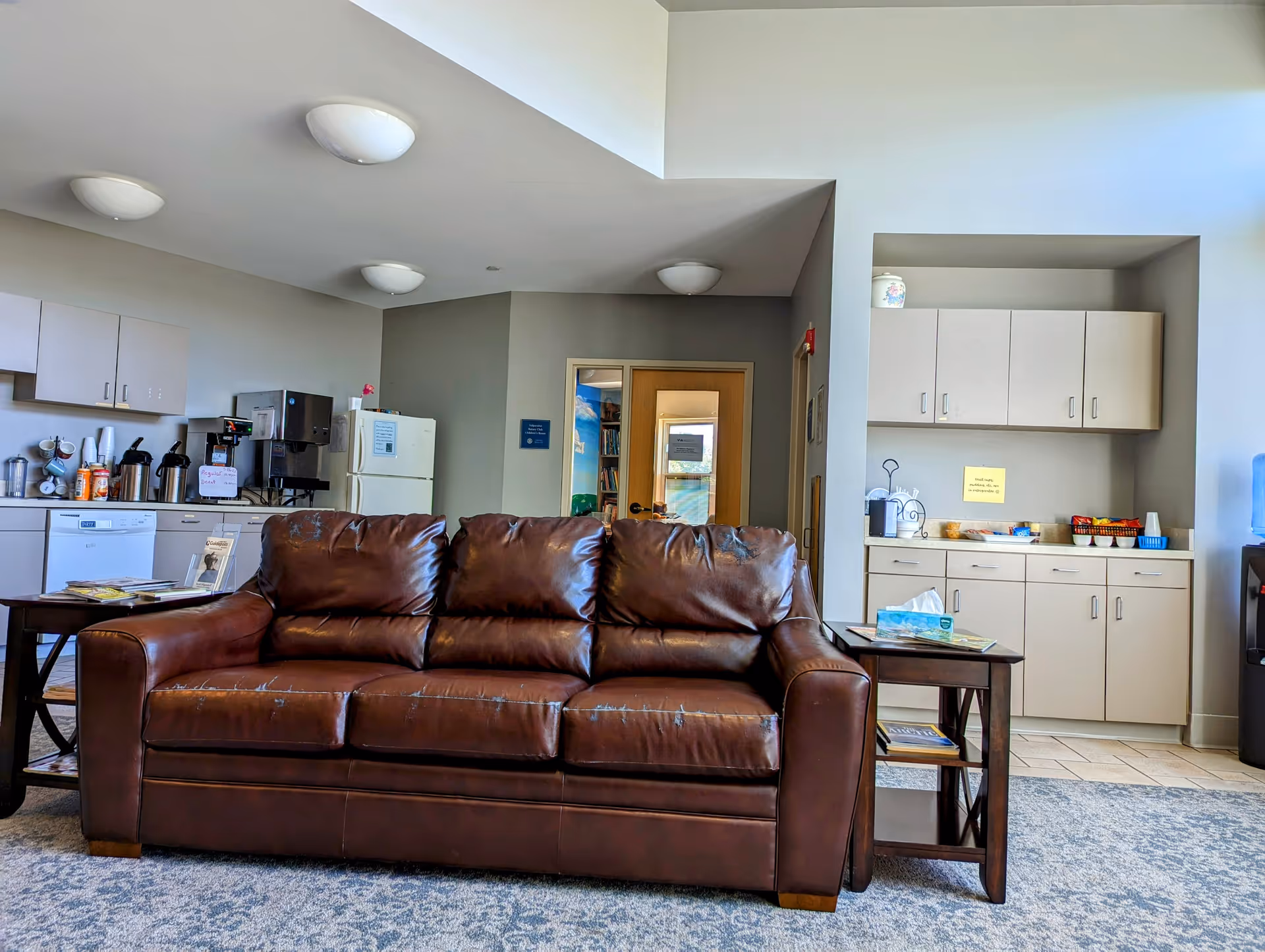 Brown leather sofa in a communal senior living lounge with kitchenette and cabinets.