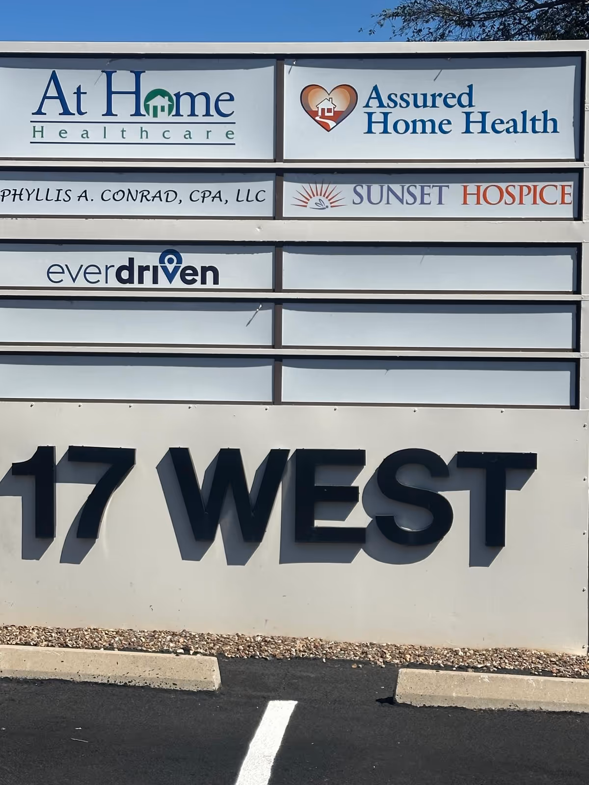 Exterior building sign featuring logos for At Home Healthcare, Assured Home Health, and Sunset Hospice.