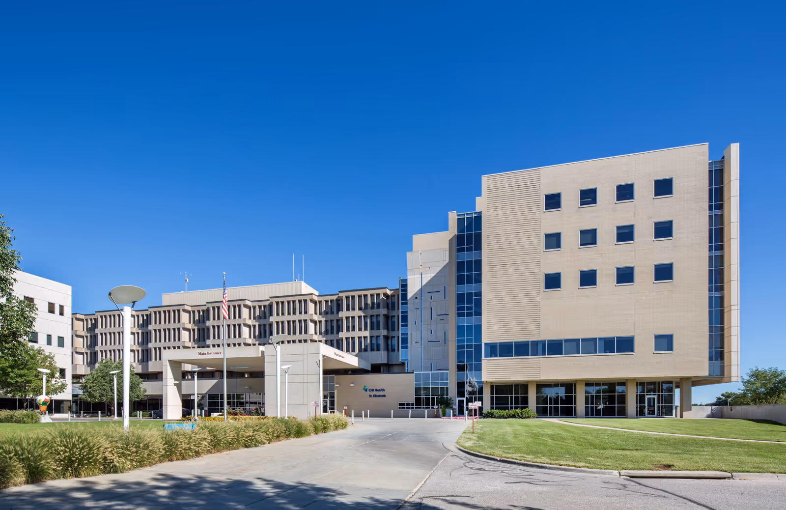 Modern medical campus building with beige facade and blue sky.