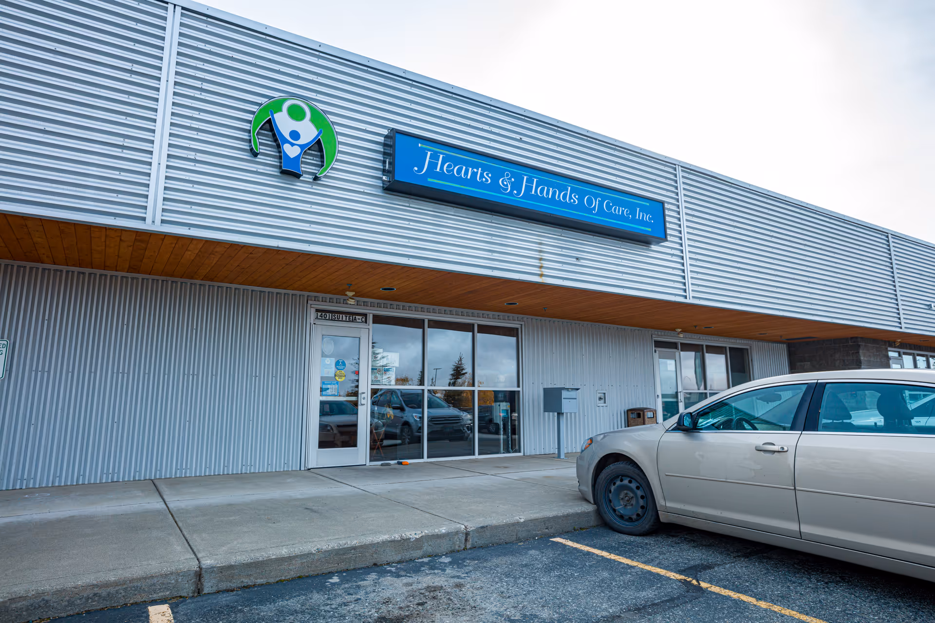 Exterior view of Heart & Hands of Care facility with entrance and parked car.