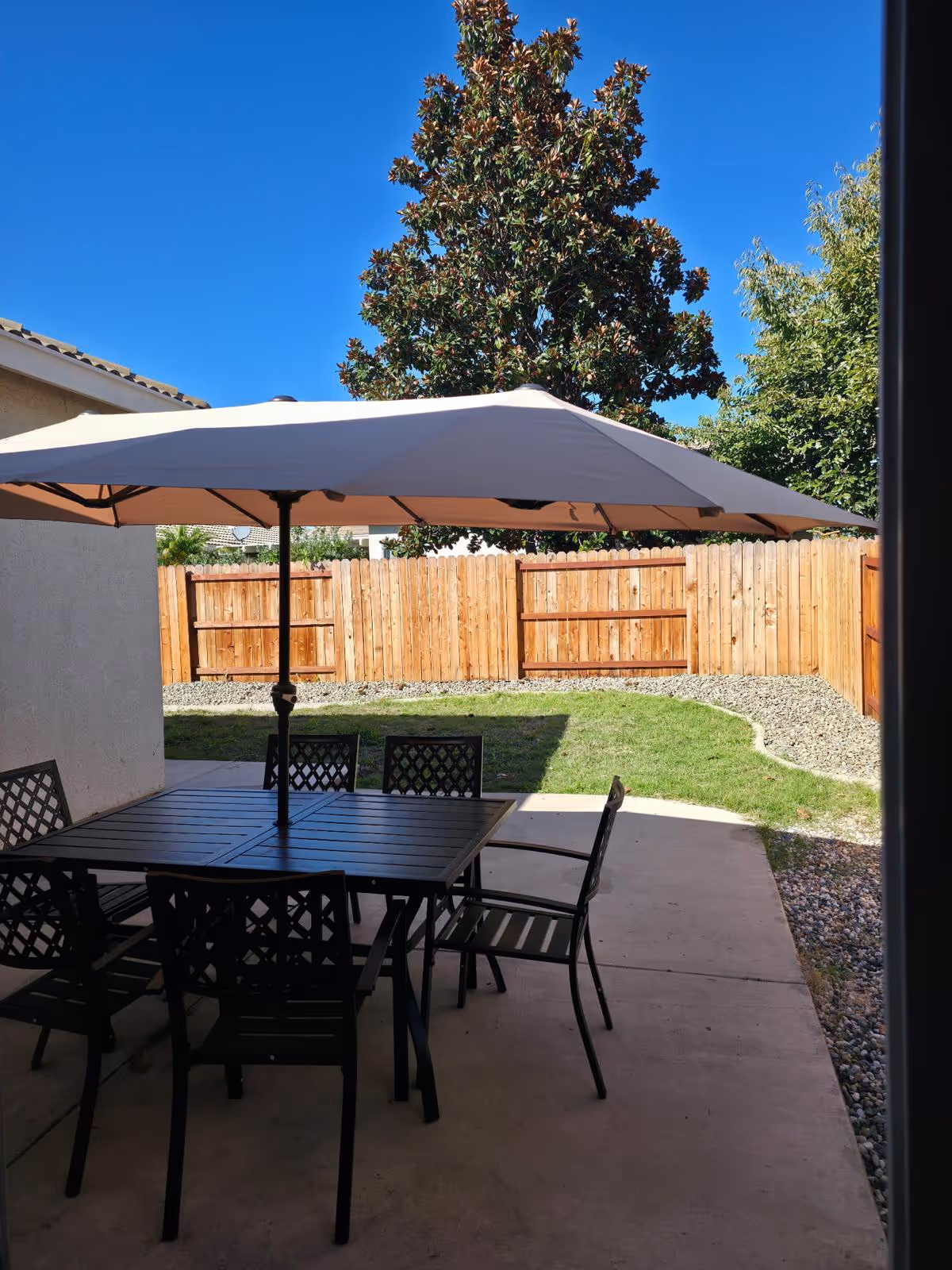 Outdoor patio with dining table, chairs, and umbrella beside a wooden fence.